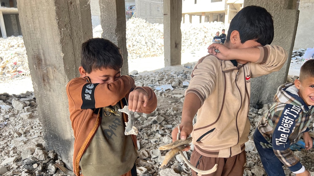 De muffe geur bij de botresten dringt door, lokale kinderen doen hun handen voor hun neus